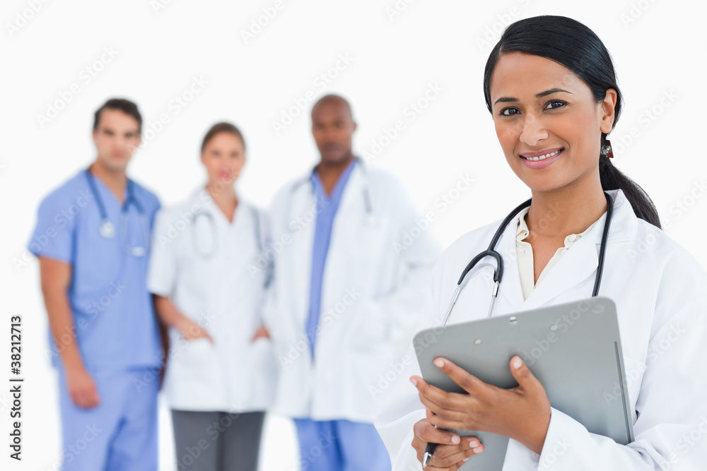 Female doctor with clipboard and staff members behind her Female doctor with clipboard and staff members behind her