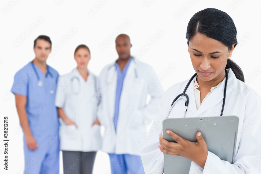 Female doctor taking notes on clipboard with staff members behin Female doctor taking notes on clipboard with staff members behin