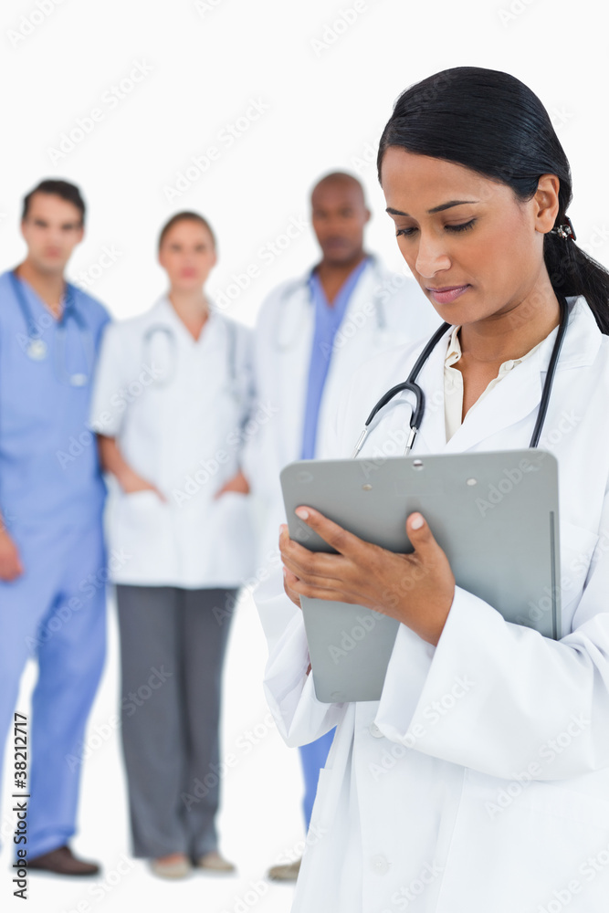 Female doctor reading notes with staff members behind her Female doctor reading notes with staff members behind her
