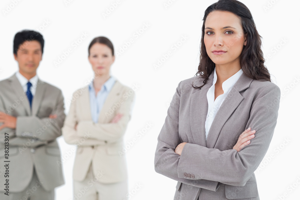 Confident saleswoman with arms folded and colleagues behind her Confident saleswoman with arms folded and colleagues behind her