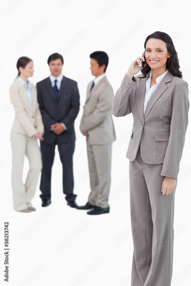 Smiling saleswoman on her cellphone with team behind her Smiling saleswoman on her cellphone with team behind her