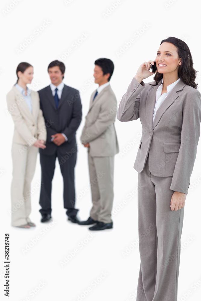 Saleswoman on the cellphone with team behind her Saleswoman on the cellphone with team behind her