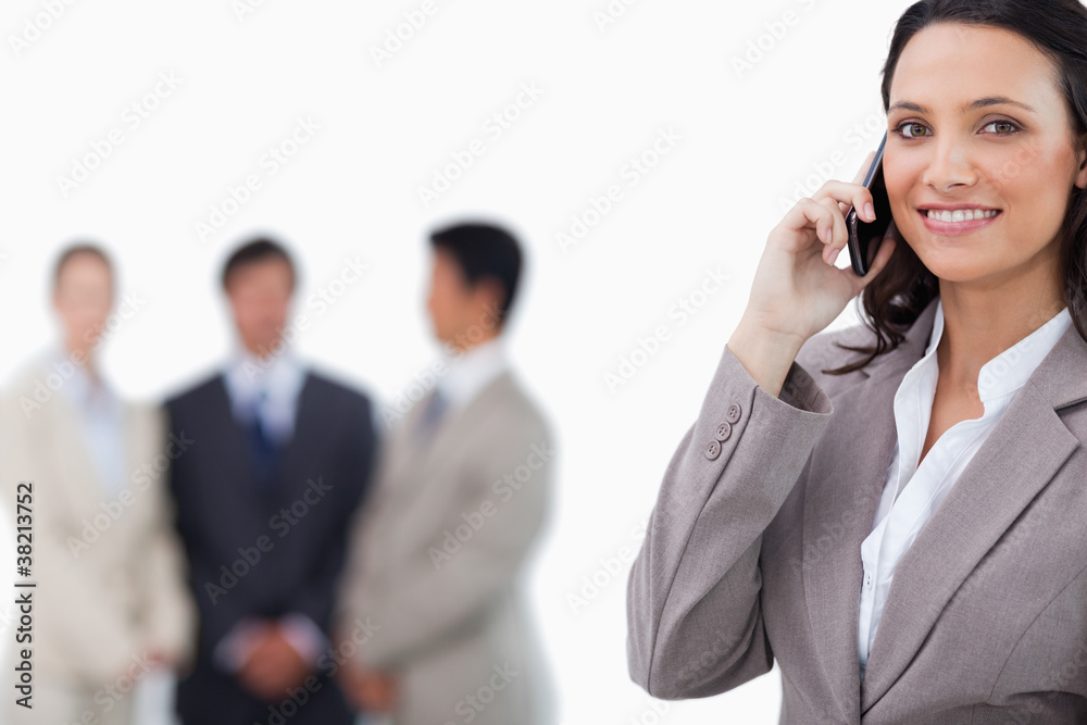 Smiling saleswoman on mobile phone with colleagues behind her Smiling saleswoman on mobile phone with colleagues behind her