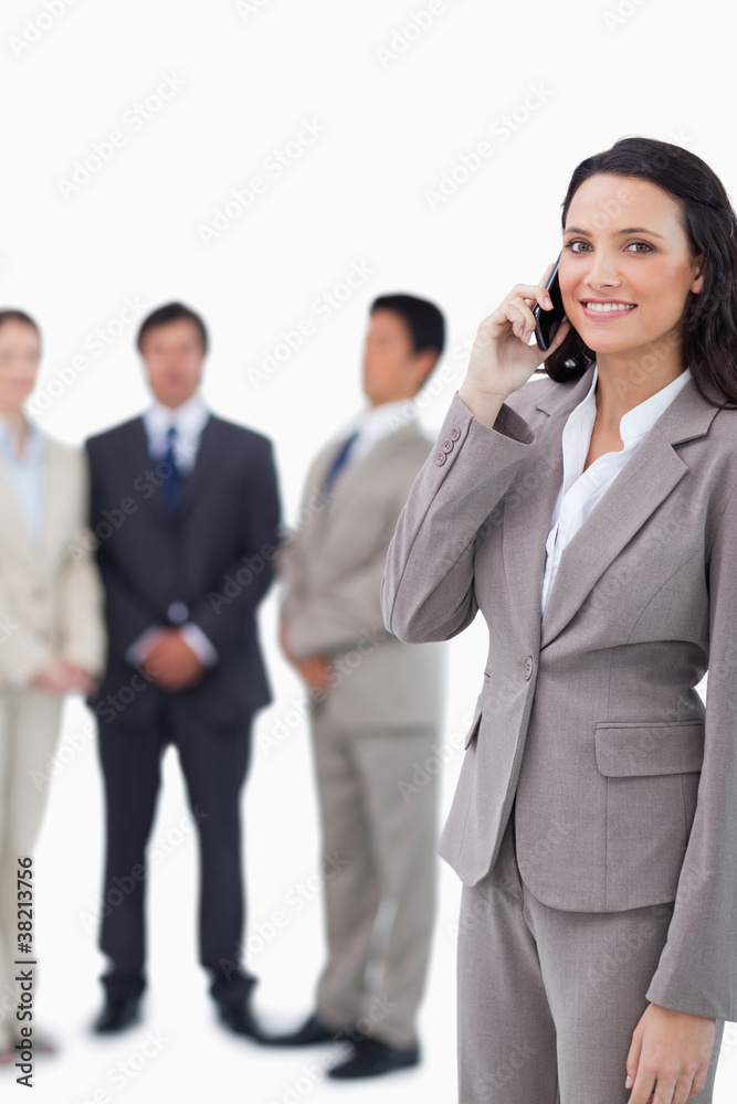 Smiling saleswoman on cellphone with team behind her Smiling saleswoman on cellphone with team behind her