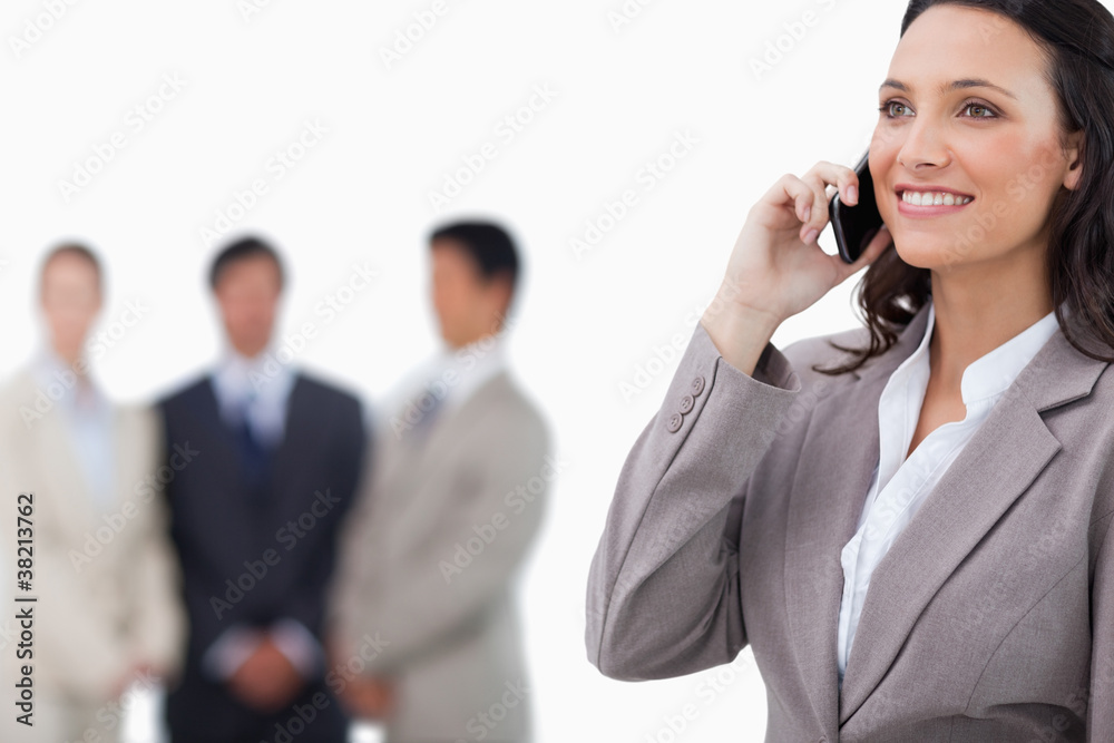 Smiling saleswoman on her mobile phone with team behind her Smiling saleswoman on her mobile phone with team behind her