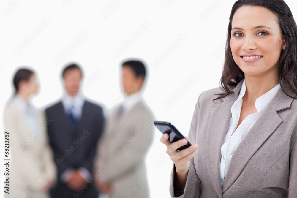 Smiling saleswoman holding cellphone with team behind her Smiling saleswoman holding cellphone with team behind her