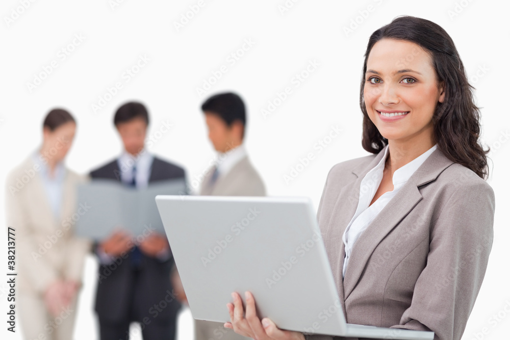 Smiling saleswoman with laptop and colleagues behind her Smiling saleswoman with laptop and colleagues behind her