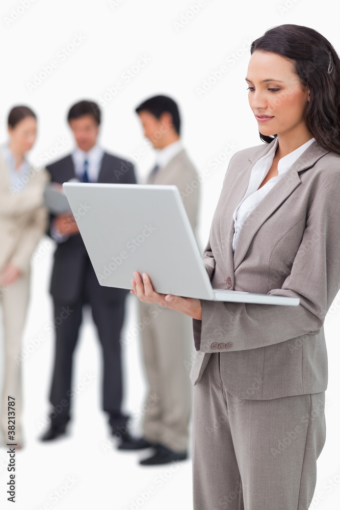 Saleswoman standing with laptop and colleagues behind her Saleswoman standing with laptop and colleagues behind her