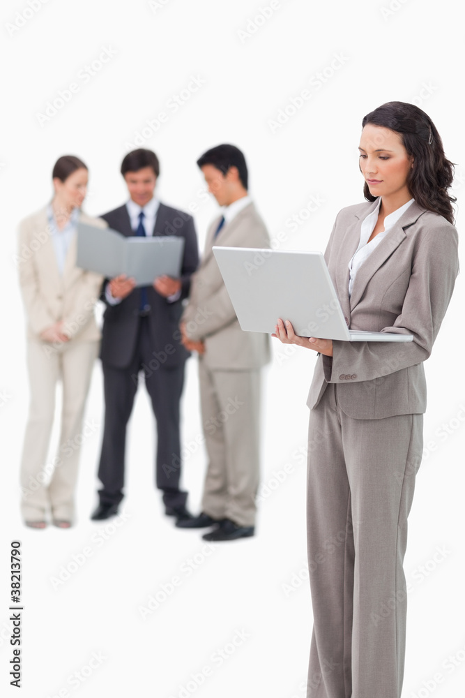 Standing saleswoman with notebook and colleagues behind her Standing saleswoman with notebook and colleagues behind her