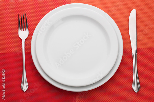 White empty plate with fork and knife on a red tablecloth
