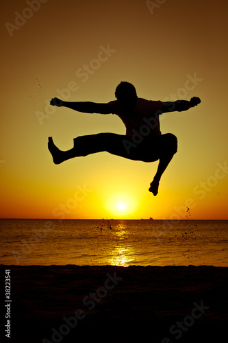 Silhouette of a man jumping on the beach at sunset