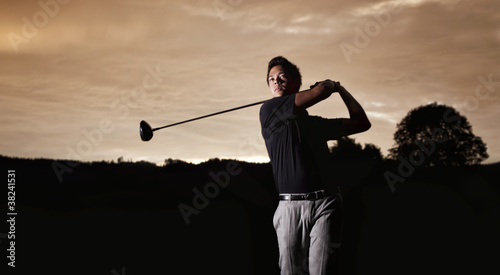 Golf player teeing off at sunset.