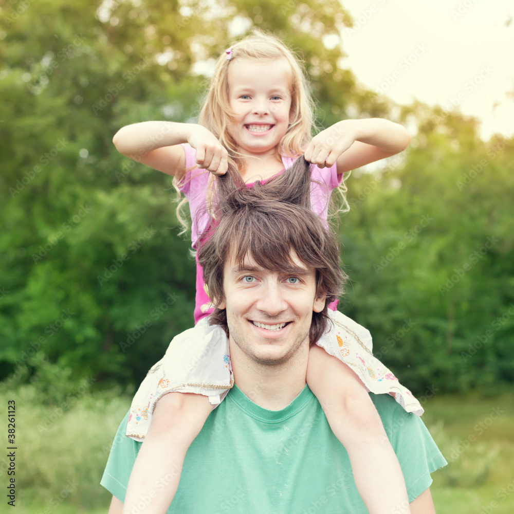 Obraz premium Young man holding blonde little girl on shoulders in park
