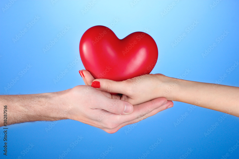 Man and woman holding red heart in hands on blue background Man and woman holding red heart in hands on blue background
