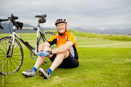 happy senior cyclist sitting on grass resting