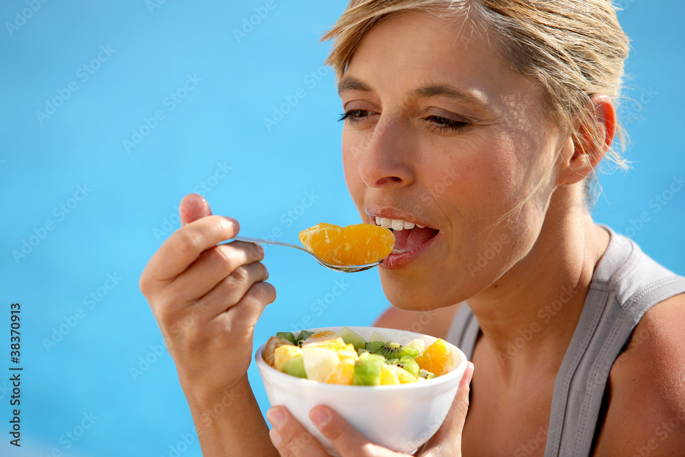 Woman eating a fruit salad by the pool