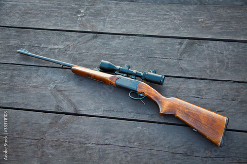 Sniper rifle with optical sight on wooden table.