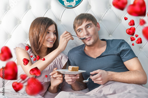 Portrait of happy couple lying in the bed. Girl feeding her boyf photo