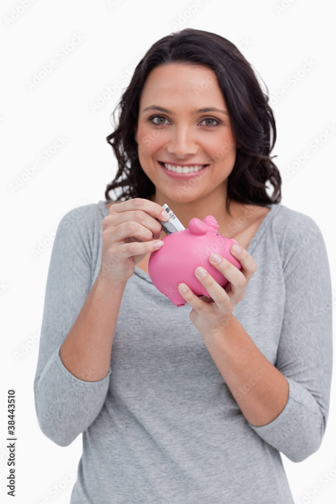 Smiling woman putting money into her piggy bank Smiling woman putting money into her piggy bank