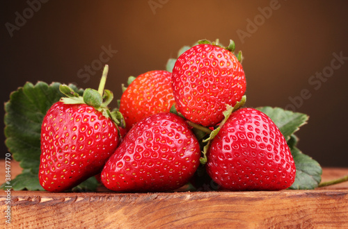 Strawberries with leaves on wooden table on brown  background