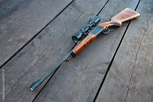 Sniper rifle with optical sight on wooden table.
