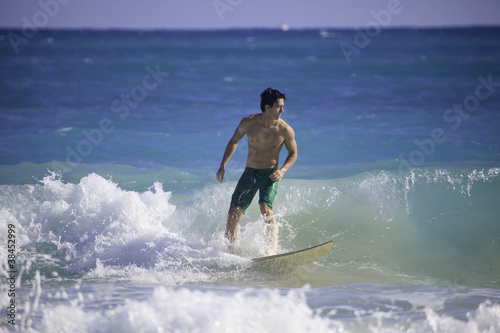 Fotomural young asian american man surfing in hawaii