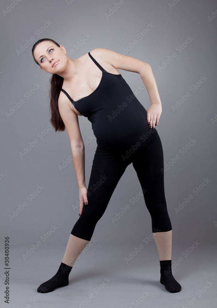 Pregnant woman doing gymnastic exercises on grey background.