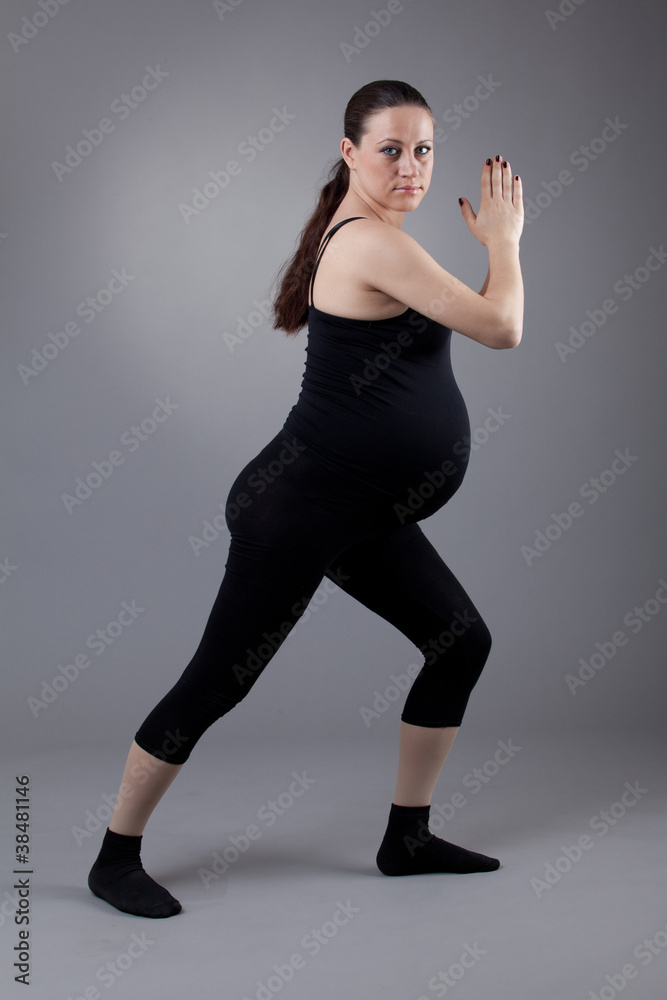 Pregnant woman doing gymnastic exercises on grey background.