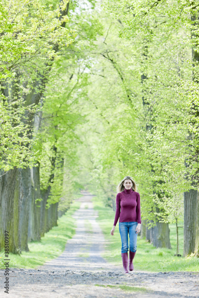 woman wearing rubber boots walking in spring alley woman wearing rubber boots walking in spring alley