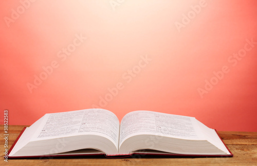 Obraz na plátne Open book on wooden table on red background