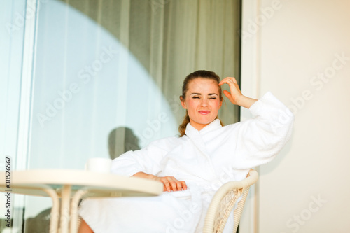 Young woman in bathrobe sitting at table on terrace