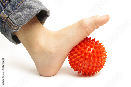 Child foot with spiny plastic orange massage ball on white backg