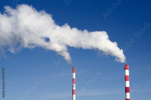 Pair of industrial chimneys with lots of smoke on a blue sky
