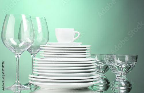 Clean plates, cup and glasses on green background
