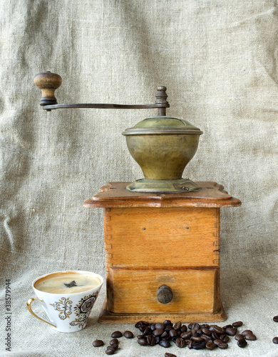 Ancient coffee grinder with grains and cup of coffee