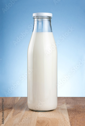 Bottle of fresh milk is wooden table on a blue background