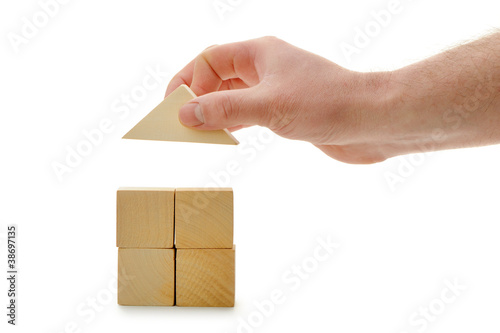 The hand establishes a toy roof on wooden cubes