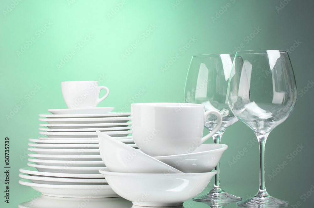 Clean plates, cups and glasses on green background