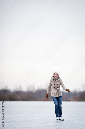 Young woman ice skating outdoors on a pond on a freezing winter © lightpoet