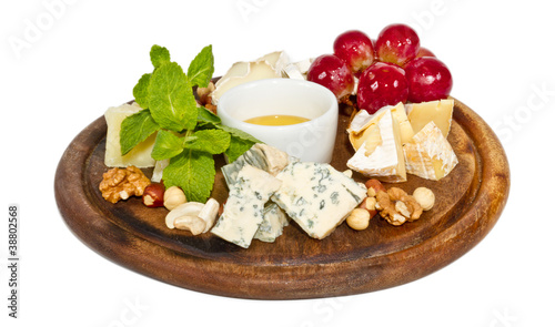 Various types of cheese with honey, nuts and grapes on plate, is