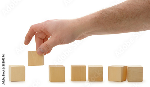 The hand establishes a wooden cube in row