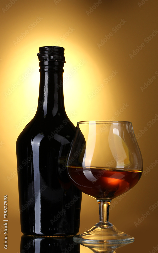 Glass of brandy and bottle on yellow background