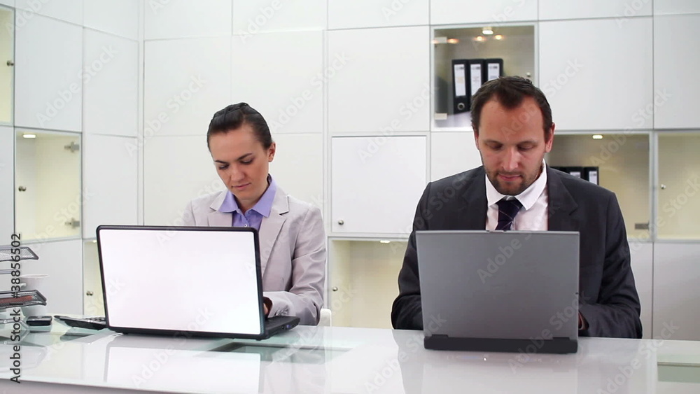 Businessman and businesswoman working on laptops in office Businessman and businesswoman working on laptops in office