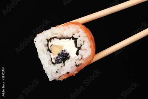 Holding roll with chopsticks isolated on black