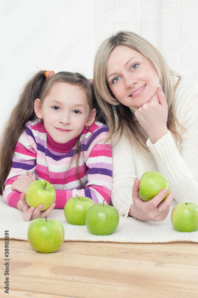 Fototapeta premium Young mother and her girl lying on the floor with green apples