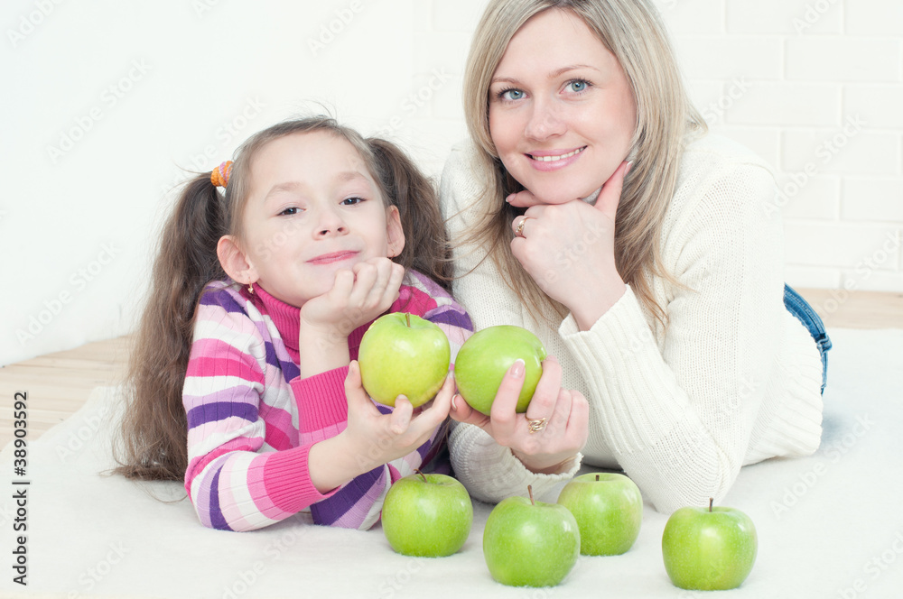 Little girl and her mother lying on the floor with green apples Little girl and her mother lying on the floor with green apples