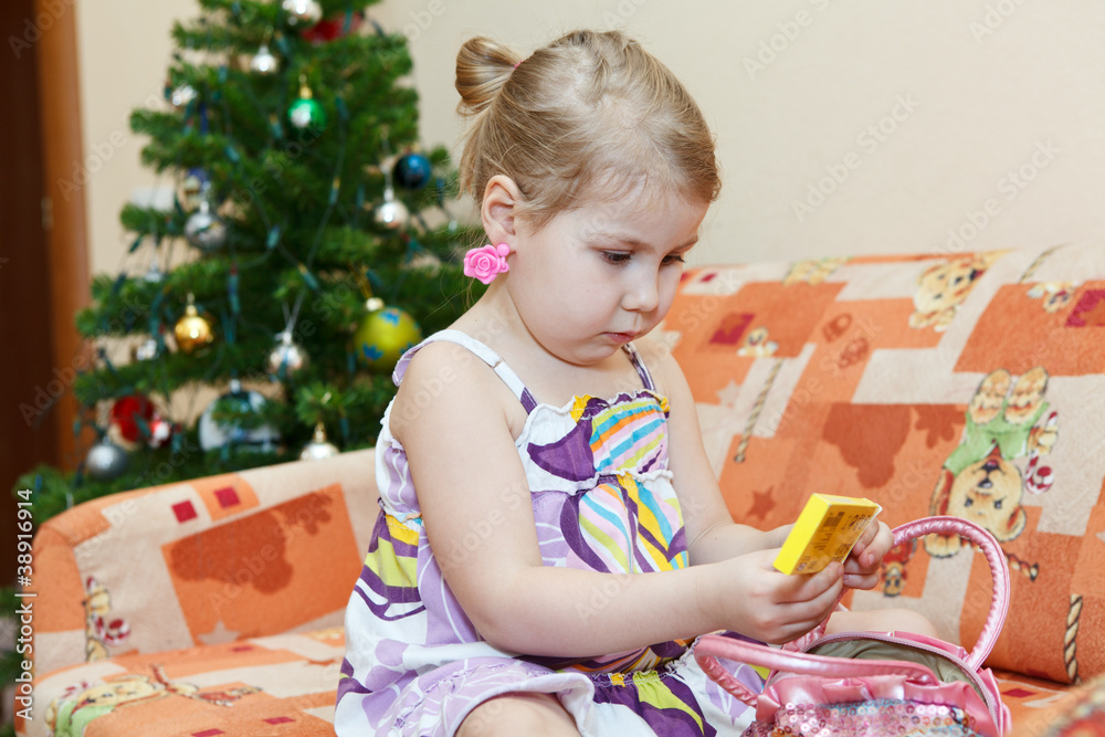 Small smiling girl sitting on couch behind christmas tree