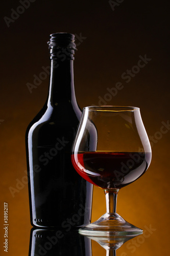 Glass of brandy and bottle on brown background