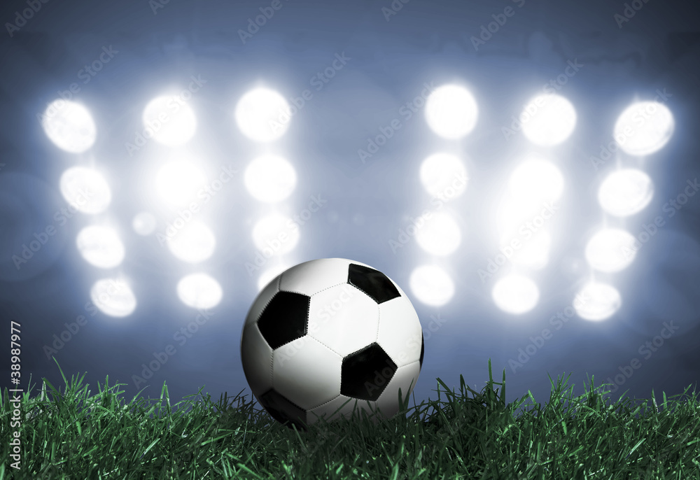 Fototapeta premium Soccer ball on grass field with spotlights