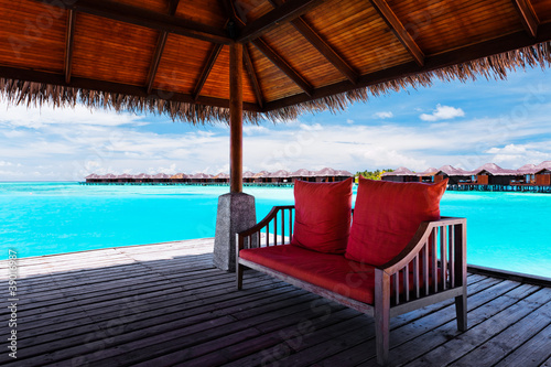 Fototapeta Naklejka Na Ścianę i Meble -  Sofa with red pillows on jetty in tropical lagoon
